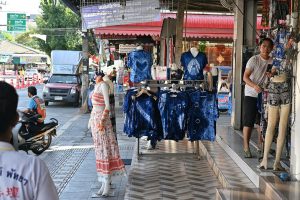 Crowds of shoppers carrying bags along a busy retail street lined with storefronts.