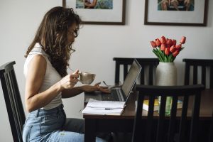 A woman writing on a laptop at home with a cup of coffee